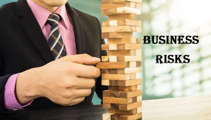 Identifying the business risks - startupstride - Startup Stride A person calculating business risks using wooden blocks, symbolizing the importance of knowing how much is business insurance for risk management.