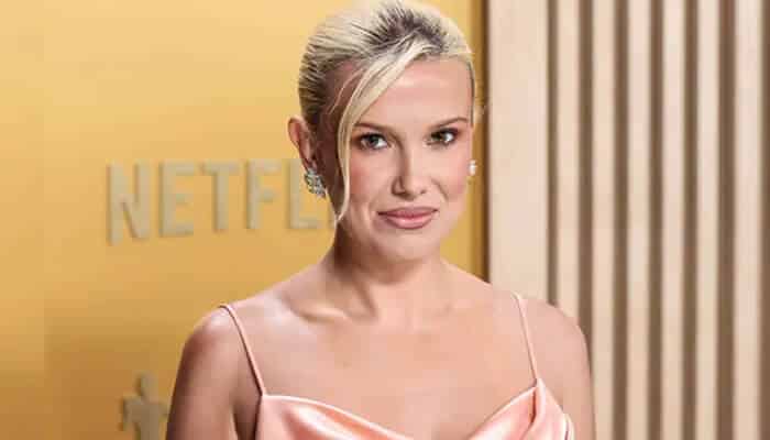Real estate investments of Millie Bobby Brown - StartupStride - Startup Stride Millie Bobby Brown posing in a peach gown at a Netflix event, highlighting her celebrity status and growing influence in the entertainment industry
