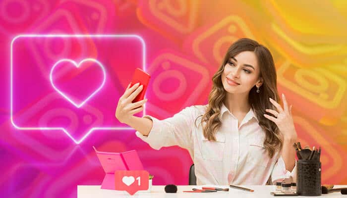 What are the things to consider before buying an Instagram photo online - Startup Stride - Startup Stride A young woman taking a selfie with a smartphone while sitting at a table with makeup products, with a glowing Instagram-like heart icon and likes symbol in the background, symbolizing social media engagement and popularity