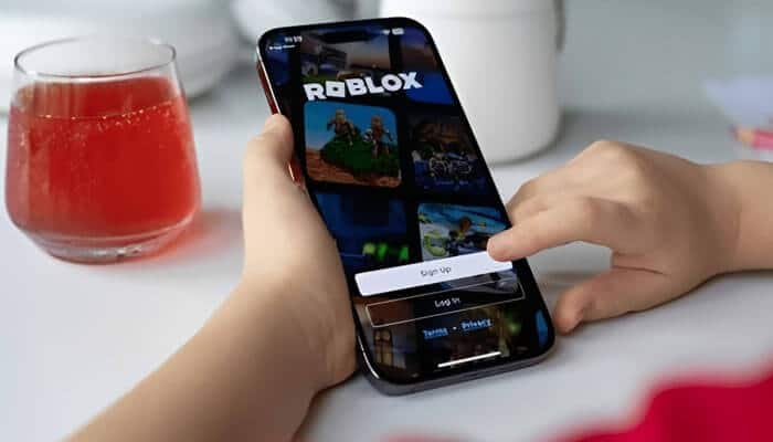 What is Robloxs phone number - Startup Stride - Startup Stride Close-up of a hand using a smartphone to access the Roblox app, with a sign-up screen visible and a drink in the background.