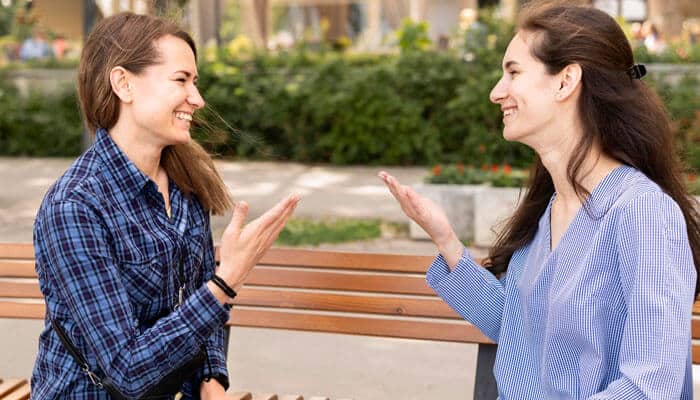 What are some questions to ask friends when bored to know about you - Stratup Stride - Startup Stride Two friends laughing and chatting on a park bench, enjoying a lighthearted conversation that reflects funny questions to ask friends when bored.